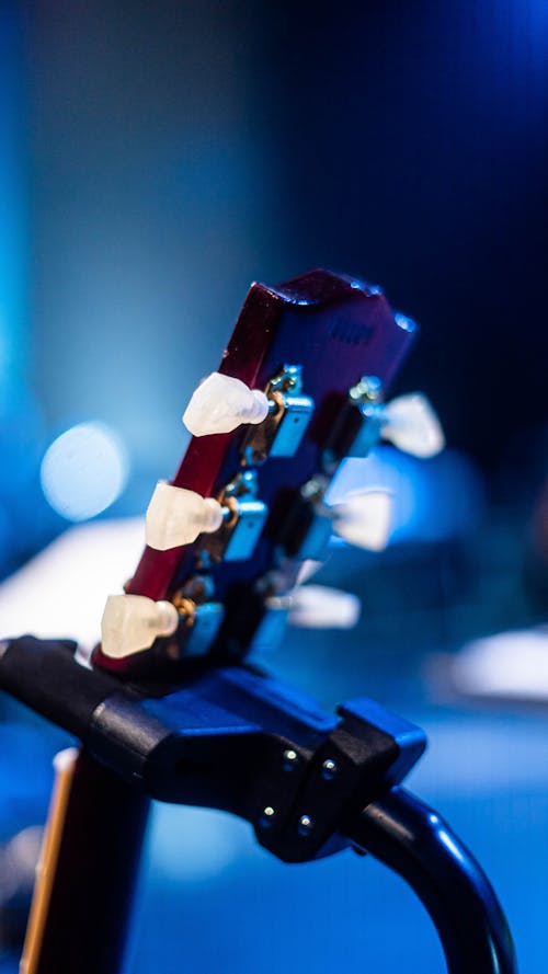 Head of modern guitar with plastic pegs placed on holder on blurred background of stage during show