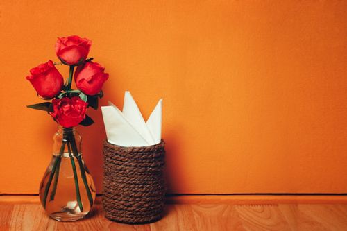 Free Charming arrangement of red roses in a vase with napkins, set against an orange background. Stock Photo
