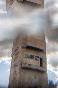 From below of aged house exterior with graffiti on rough walls reflecting in sky with clouds