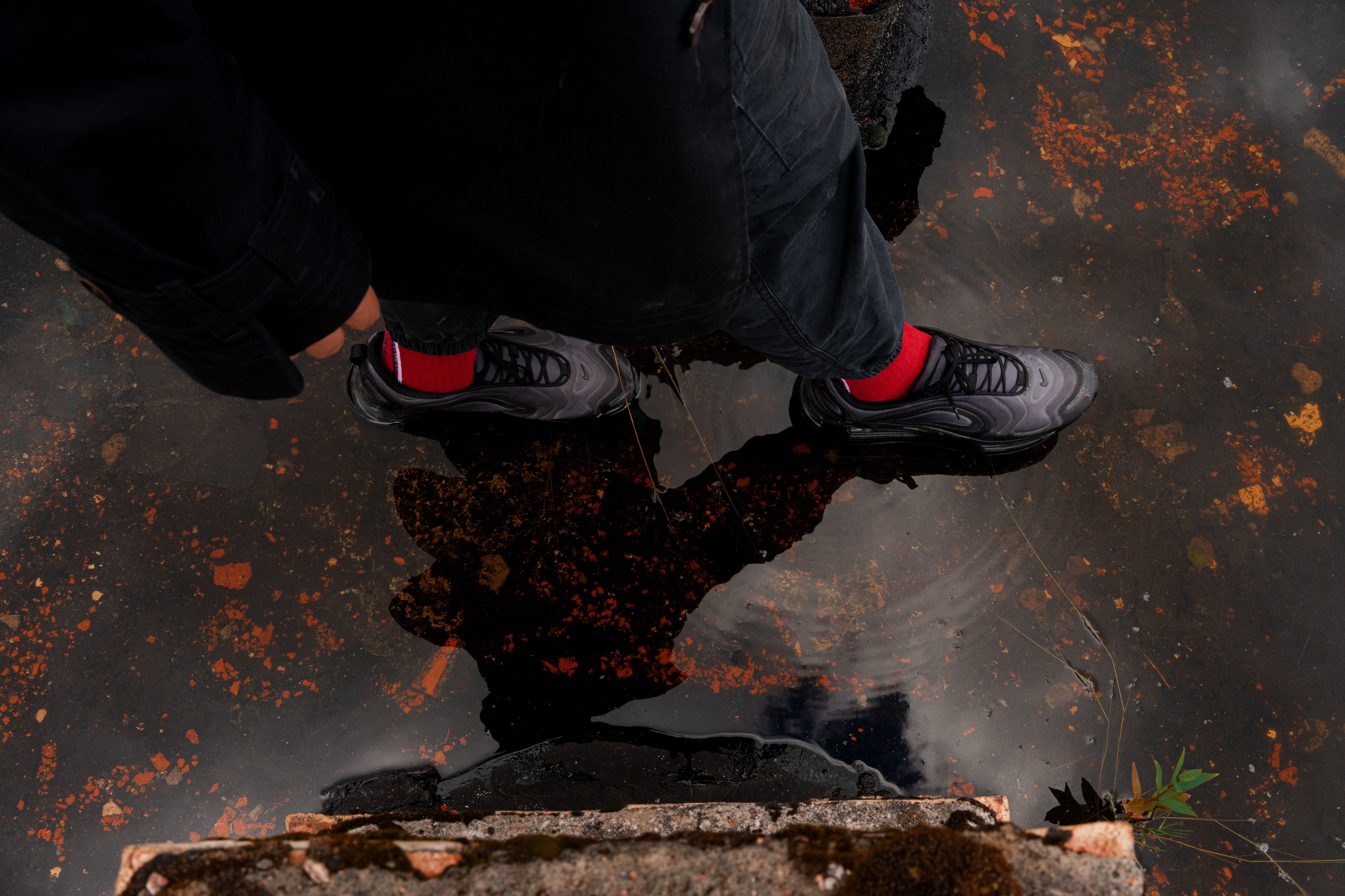 From above of crop unrecognizable person in stylish apparel strolling on icy puddle with faded leaves in fall