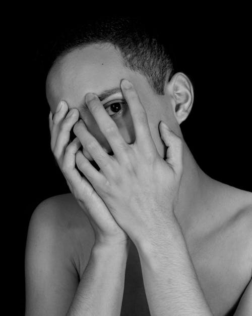 Grayscale Photo of a Topless Man Covering His Face on Plain Black Background