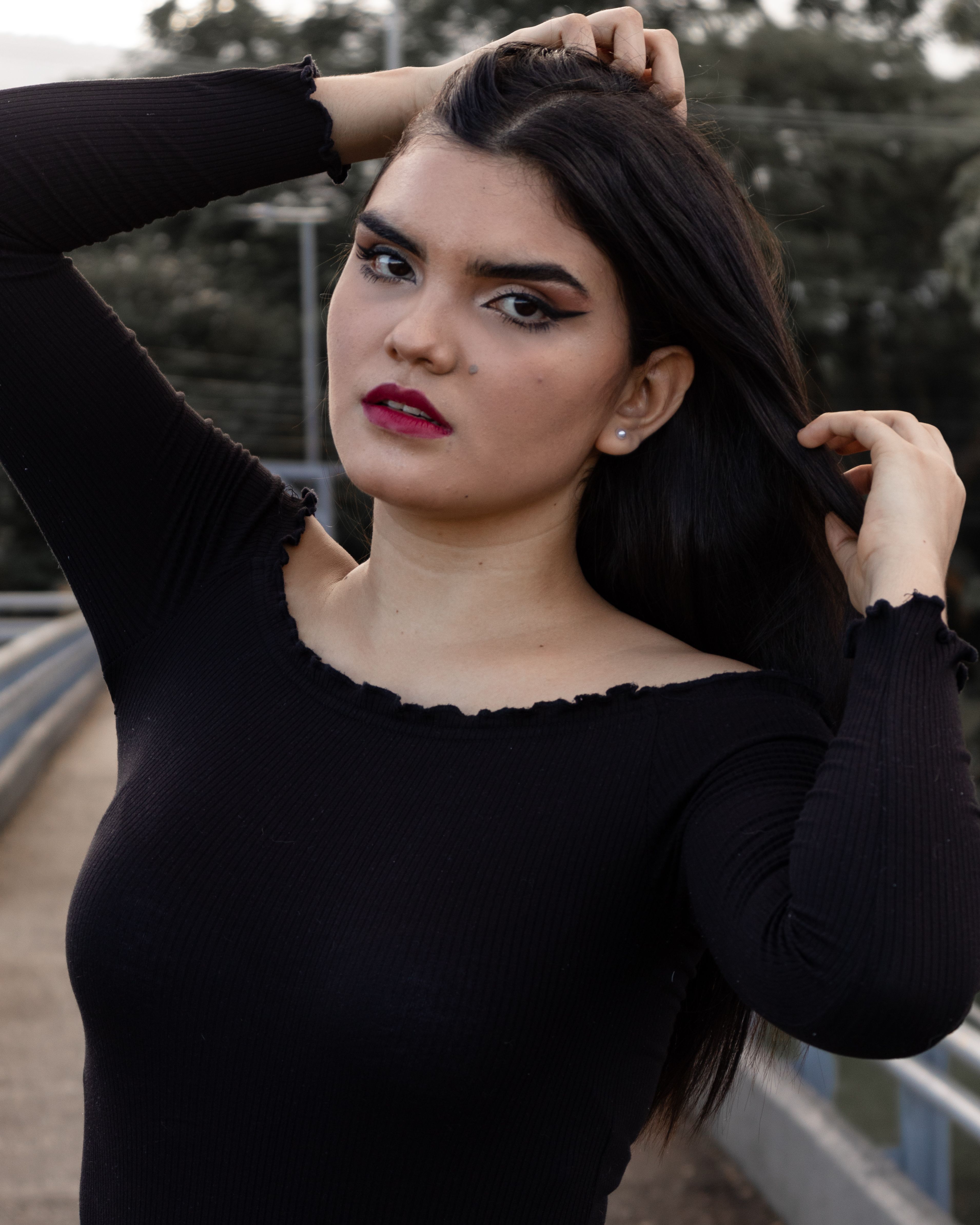 A striking portrait of a woman in black long sleeves posing outdoors, fixing her hair.