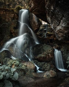 A serene waterfall flows over mossy rocks in a lush forest setting, showcasing nature's beauty.