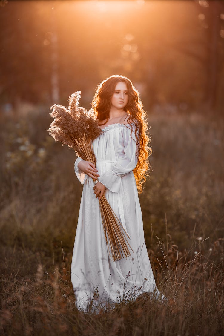 Woman With Flowers In Field At Sunset