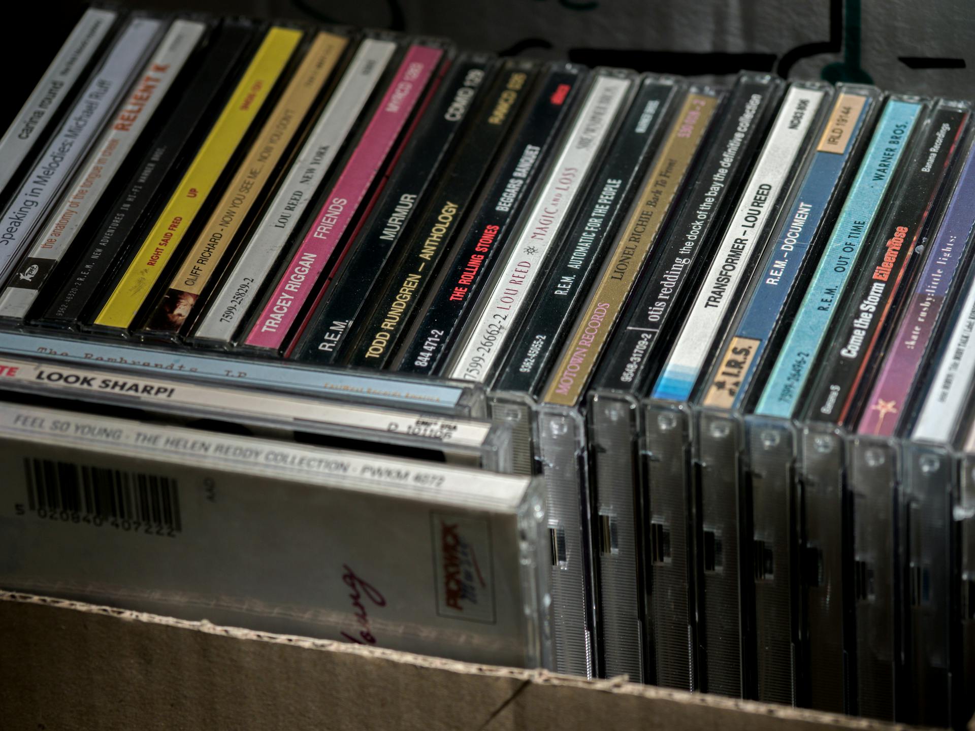 Close-up image of various music CDs in cases organized in a box, showing titles and artists.