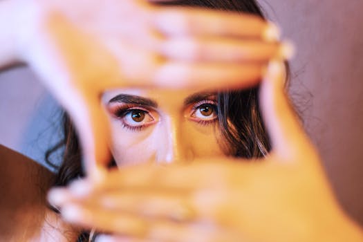 Artistic close-up of a woman's face framed by her hands, showcasing expressive eyes and creative makeup.