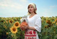 Young woman in country outfit with clay jug in sunflower field in sunny summer day
