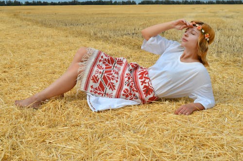 Calm female in traditional Russian clothes lying on dry grass with closed eyes and relaxing