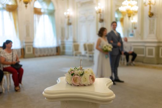 Blooming flower decoration on table in hall with shiny chandeliers above anonymous bride and groom on wedding day