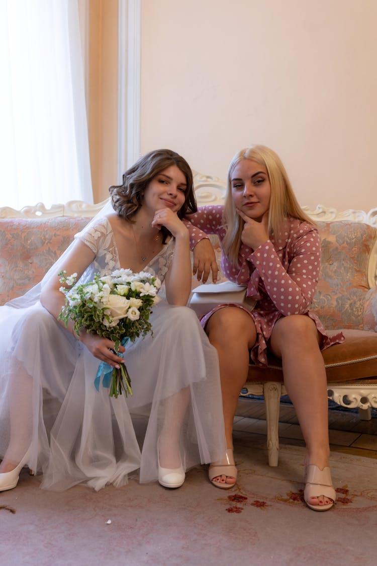 Trendy Bride With Flowers Near Bridesmaid On Sofa