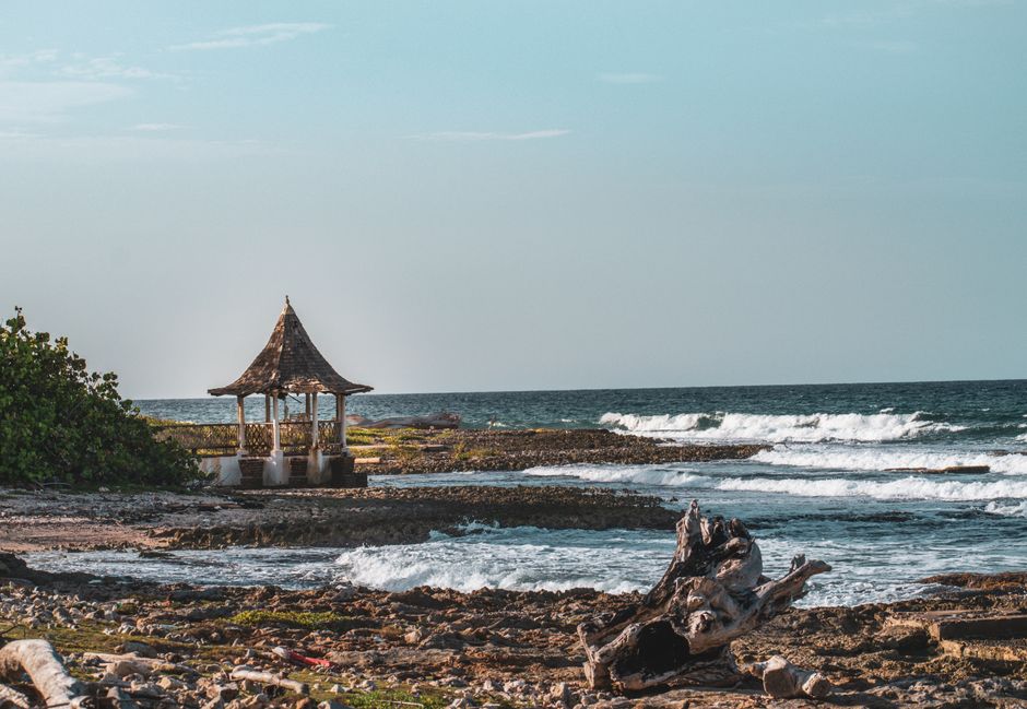 A picturesque beach scene with a gazebo by the sea, featuring waves crashing on a rocky shore.