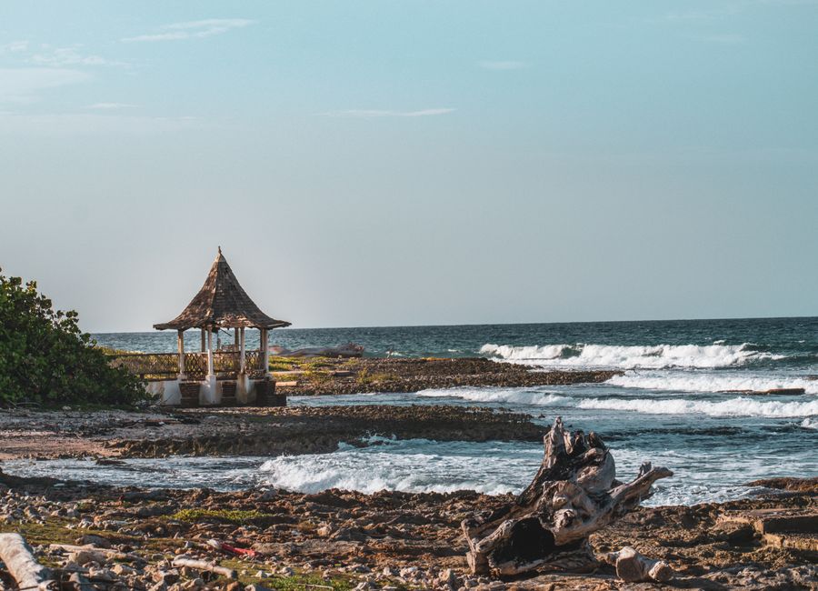 A picturesque beach scene with a gazebo by the sea, featuring waves crashing on a rocky shore.