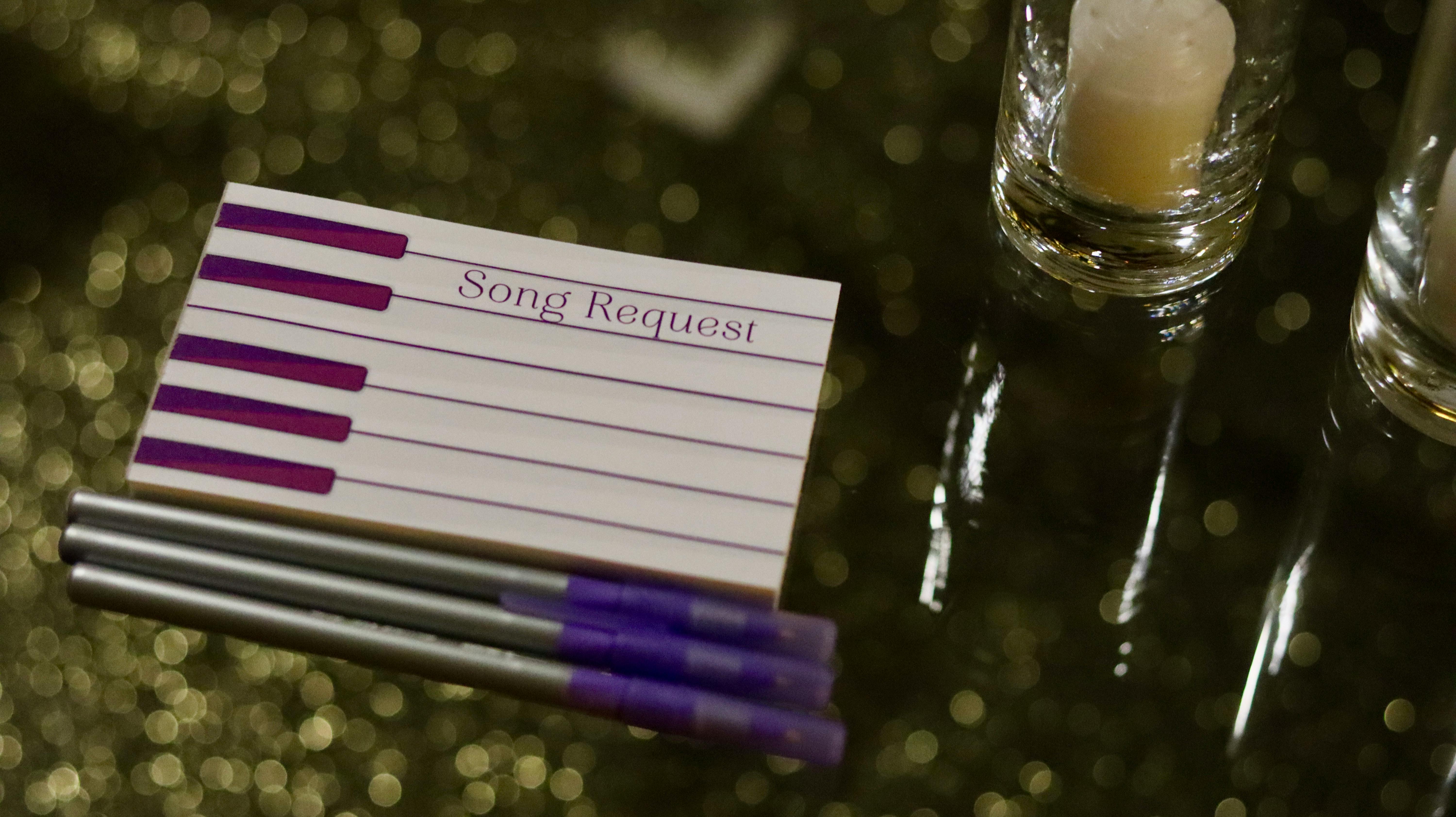 Close-up of song request cards with pens and lit candles, perfect for events.