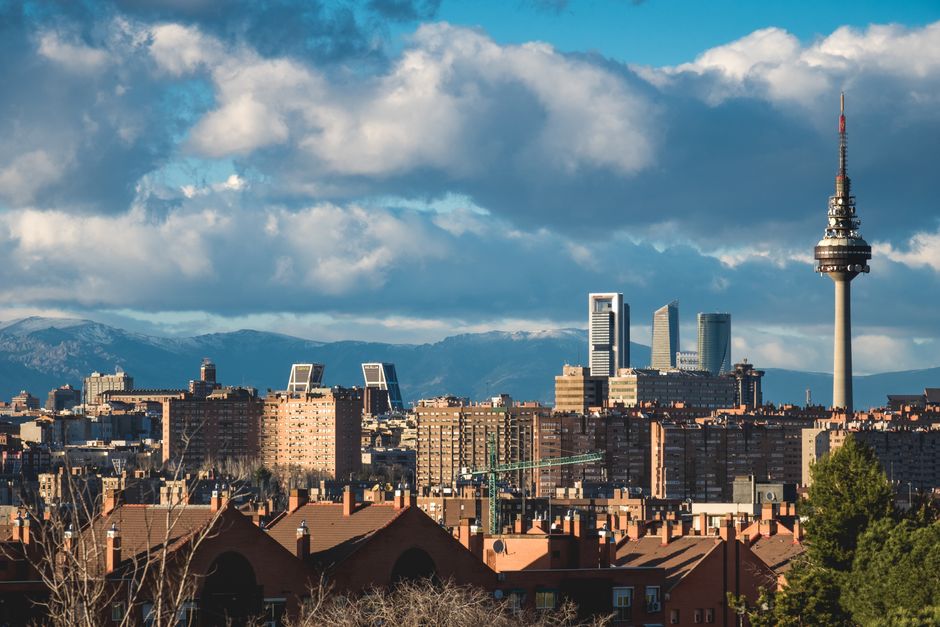 Explore the vibrant skyline of Madrid featuring the iconic Torrespaña Tower with a backdrop of mountains and city architecture.