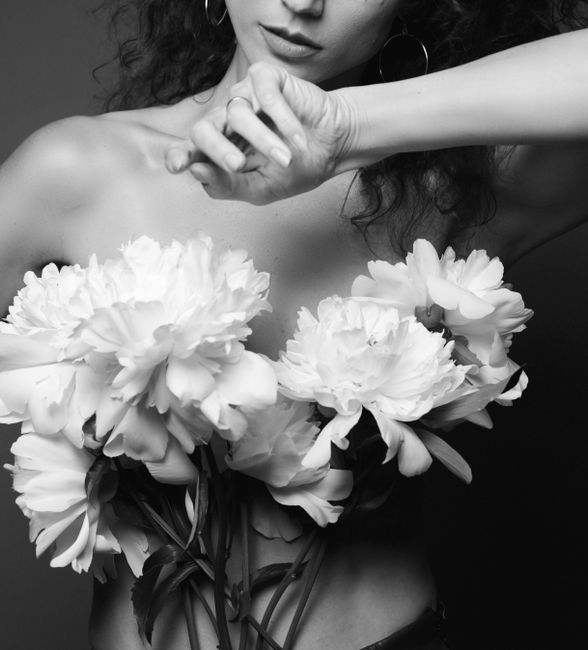 Black and white of crop anonymous naked alluring female with long dark hair covering breast with delicate peonies