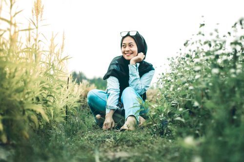 Free Beautiful woman in hijab smiling while sitting in a grass field, enjoying a sunny day outdoors. Stock Photo