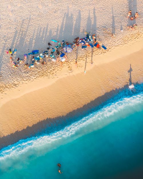 Free Top-down view of a sandy beach with tourists, colorful towels, and vivid blue ocean waves. Stock Photo