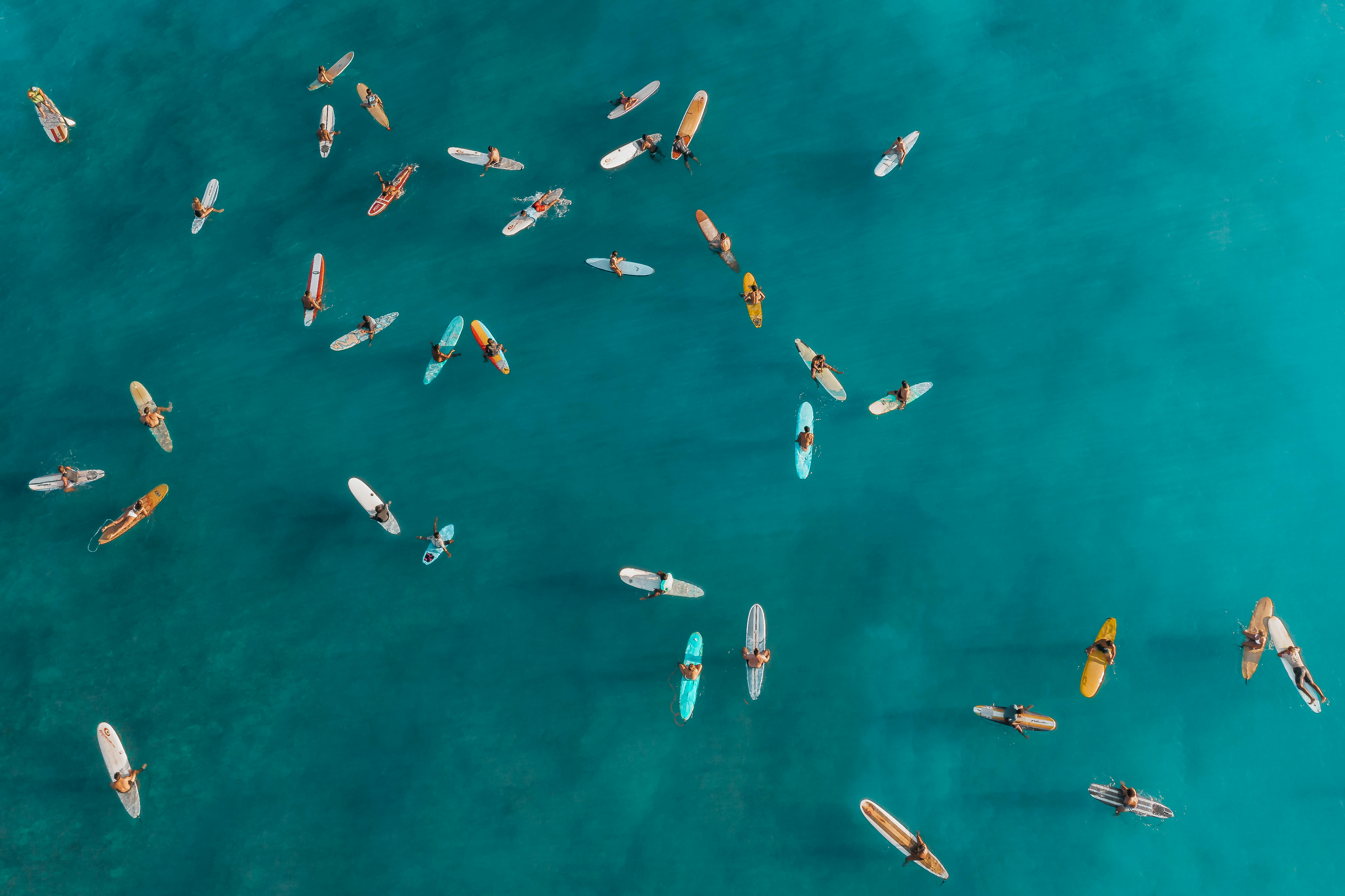无人机捕捉到了在热带海域冲浪板上等待的冲浪者，周围环绕着碧绿色的海浪