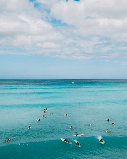 Free Aerial view of surfers in bright blue ocean catching waves under a cloudy sky. Stock Photo