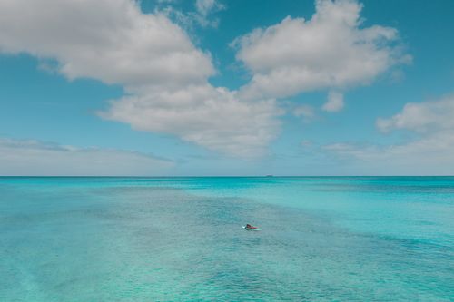 Free A lone paddleboarder on a turquoise sea under a bright blue sky with fluffy clouds, perfect for summer travel vibes. Stock Photo