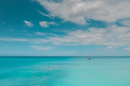 Idyllic clear blue ocean with paddleboarders and distant boat under a bright sky.