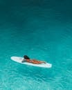 Woman in Black Bikini Lying on White Surfboard on Water