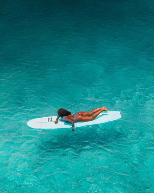 Free Aerial view of a woman on a surfboard in a clear turquoise ocean, embodying leisure and tranquility. Stock Photo