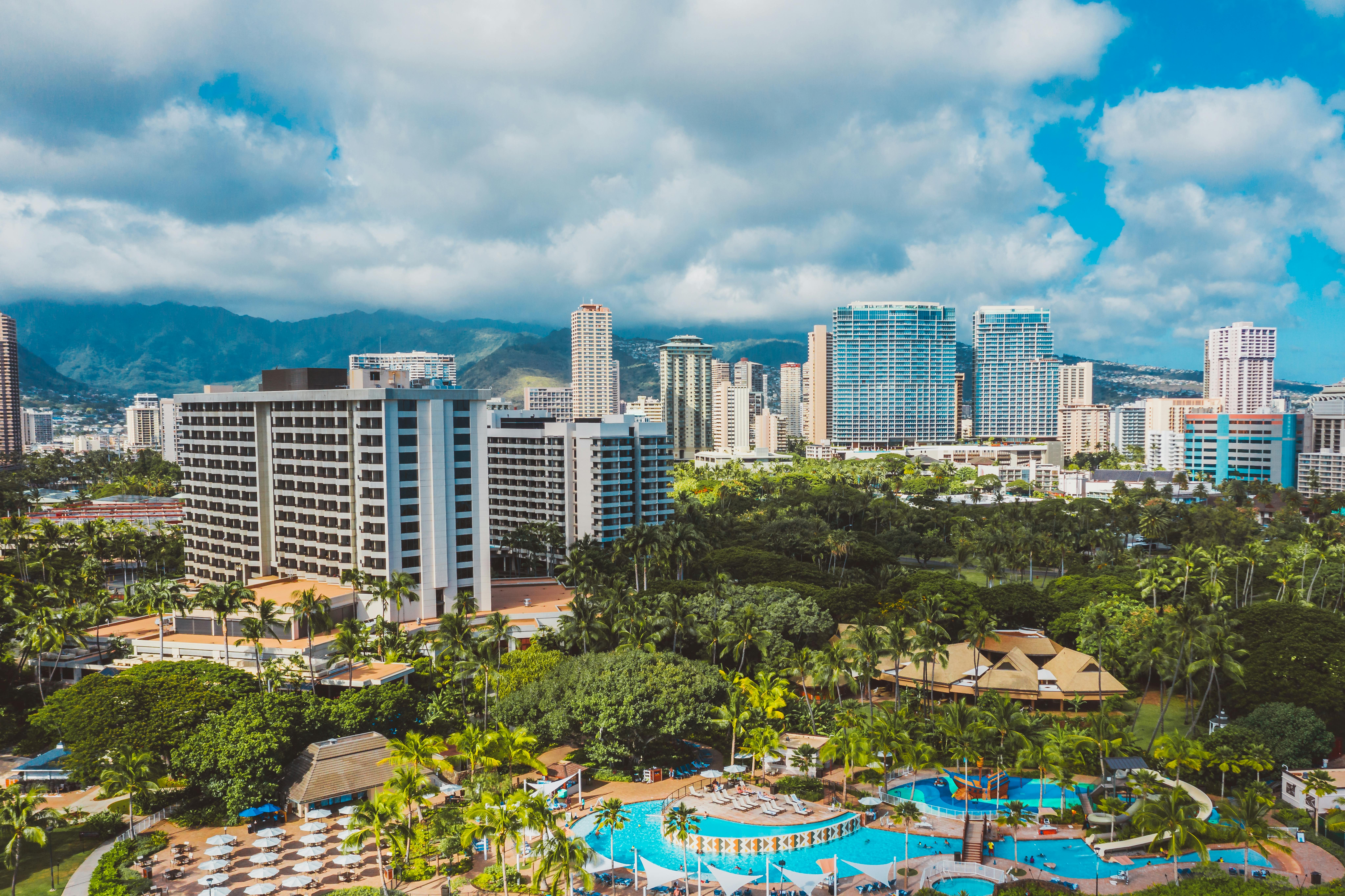 Stunning aerial view of Honolulu's skyline and resort pools with lush greenery and mountains.