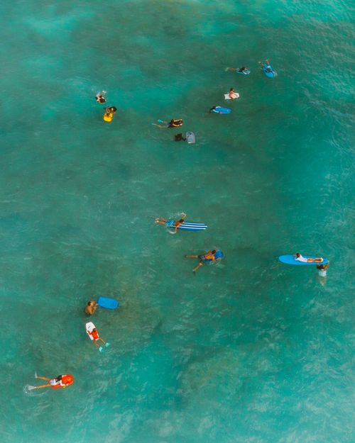 Free Aerial shot capturing a group of surfers floating on their boards in clear tropical ocean waters. Stock Photo