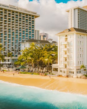 Luxury tropical beachfront hotels with palm trees and golden sand under a bright sky.
