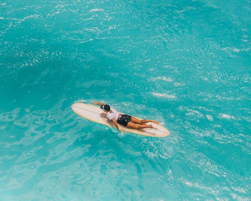Woman in Black Shorts Lying on White Surfboard on Water