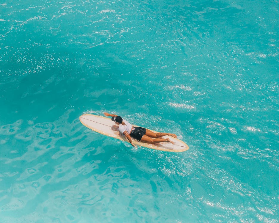 Woman in Black Shorts Lying on White Surfboard on Water