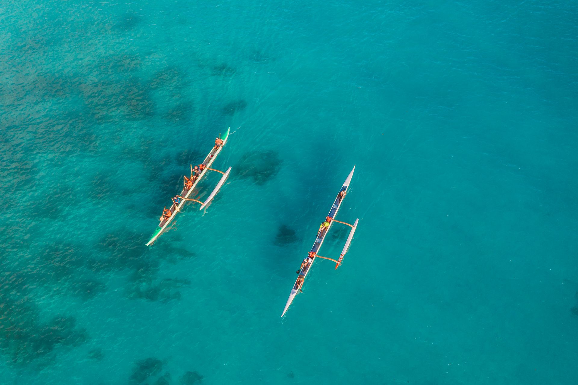 Two canoes with people paddling in clear, tropical turquoise waters.