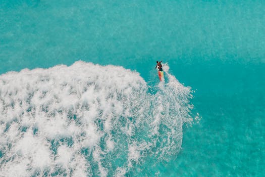 A surfer skillfully rides a turquoise wave, captured from above, showcasing the excitement of surfing.