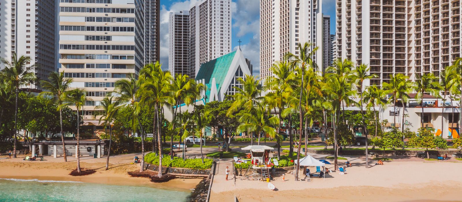 Explore the vibrant Honolulu coastline with skyscrapers, palm trees, and a sandy beach under a sunny sky. — flights from Seattle to Honolulu