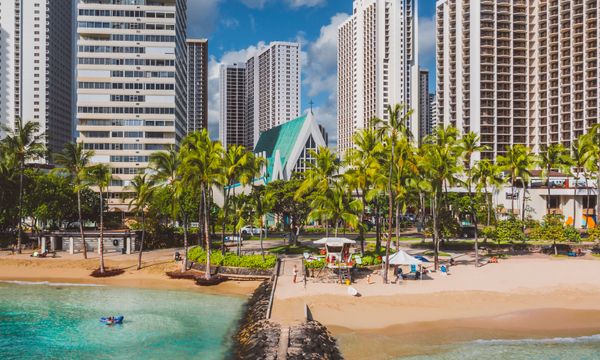 Explore the vibrant Honolulu coastline with skyscrapers, palm trees, and a sandy beach under a sunny sky.