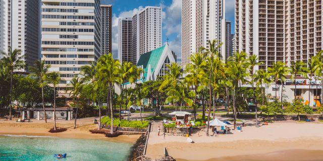 Explore the vibrant Honolulu coastline with skyscrapers, palm trees, and a sandy beach under a sunny sky.