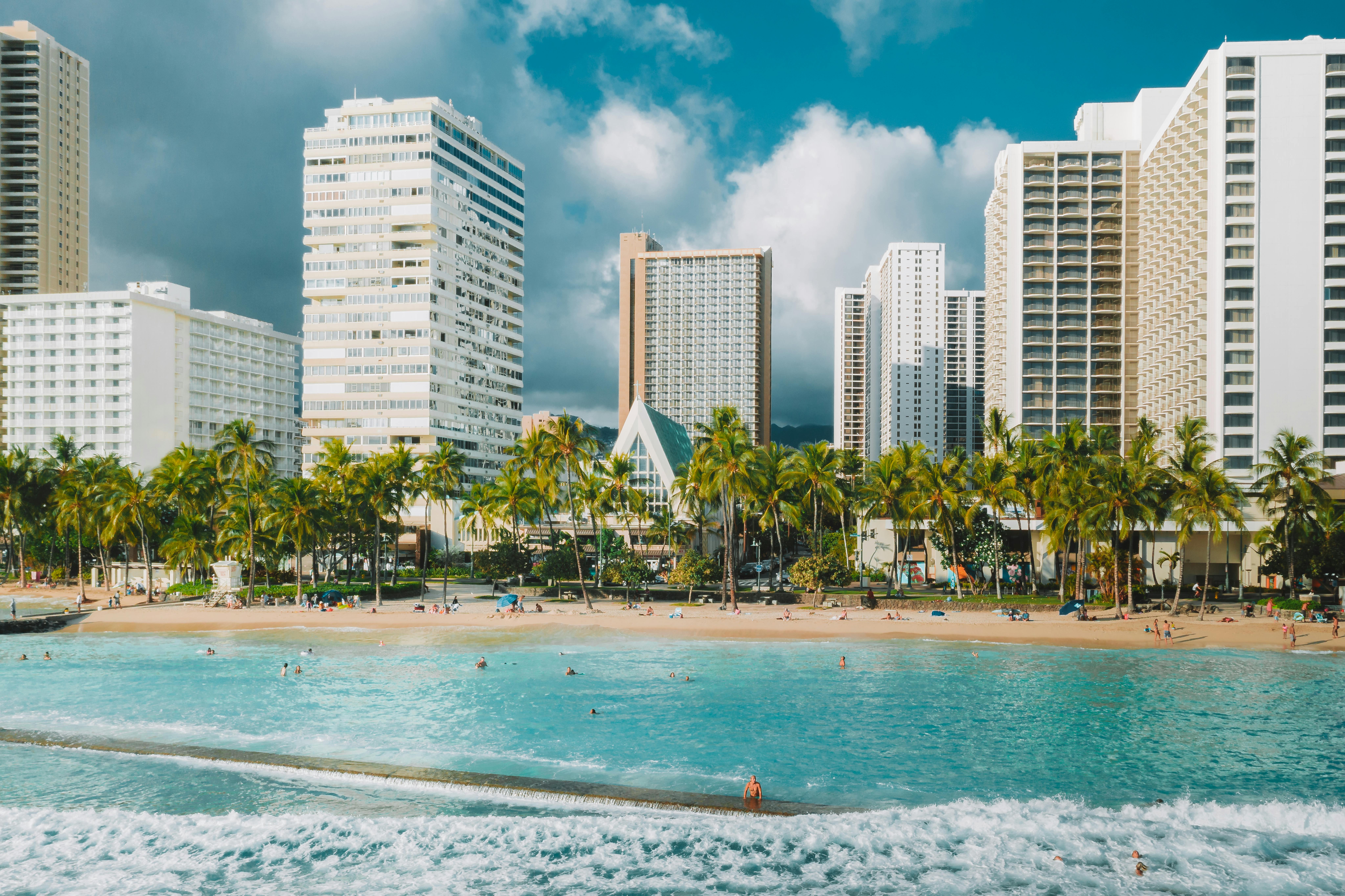Aerial view of a beach resort with turquoise waters and palm trees under a bright sky.