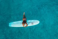Person in Black Wet Suit Riding White Surfboard on Blue Water