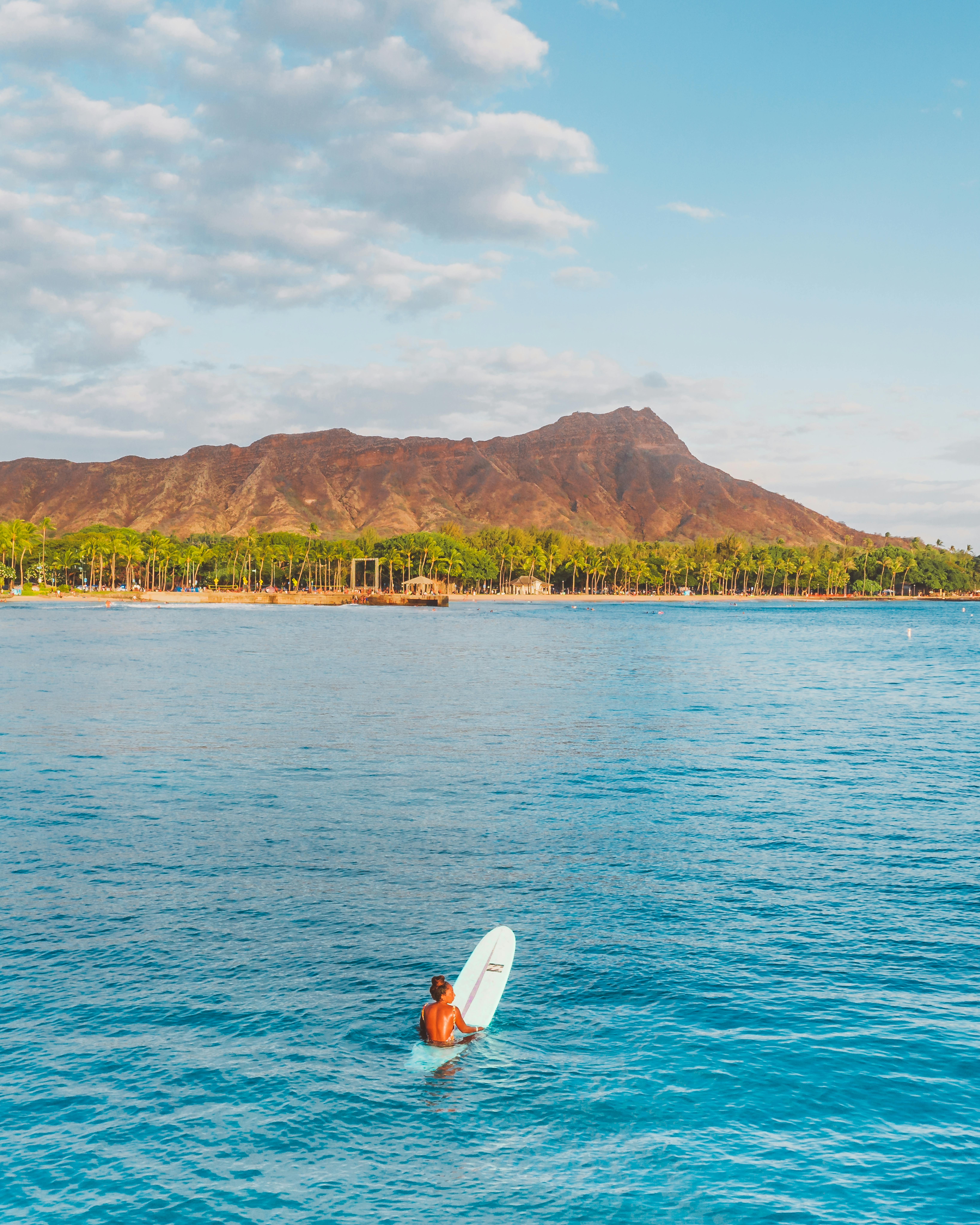 在夏威夷瓦胡岛，一位孤独的冲浪者置身于宁静的蓝色海洋中，背景是钻石头火山