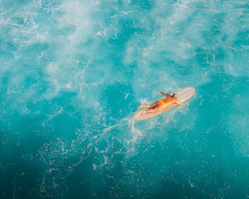 Woman Swimming on Surfboard Across Turquoise Water