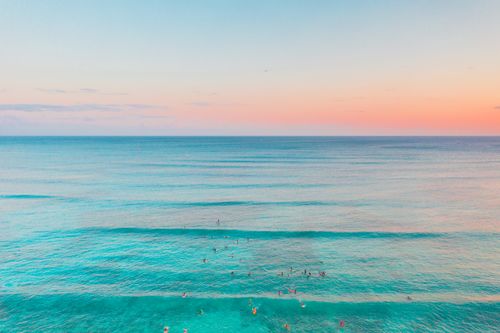 Free A stunning aerial shot capturing people swimming in turquoise ocean waves under a colorful sky. Stock Photo