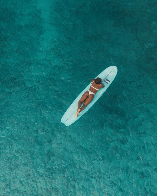 Free Aerial view of a woman in a bikini lying on a paddleboard in clear turquoise sea water, summer leisure. Stock Photo