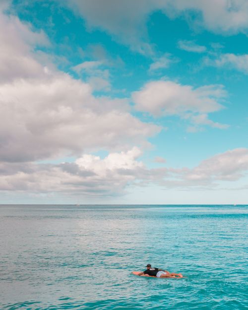 Free A surfer floats on a surfboard under a clear sky, enjoying a serene day in the ocean. Stock Photo