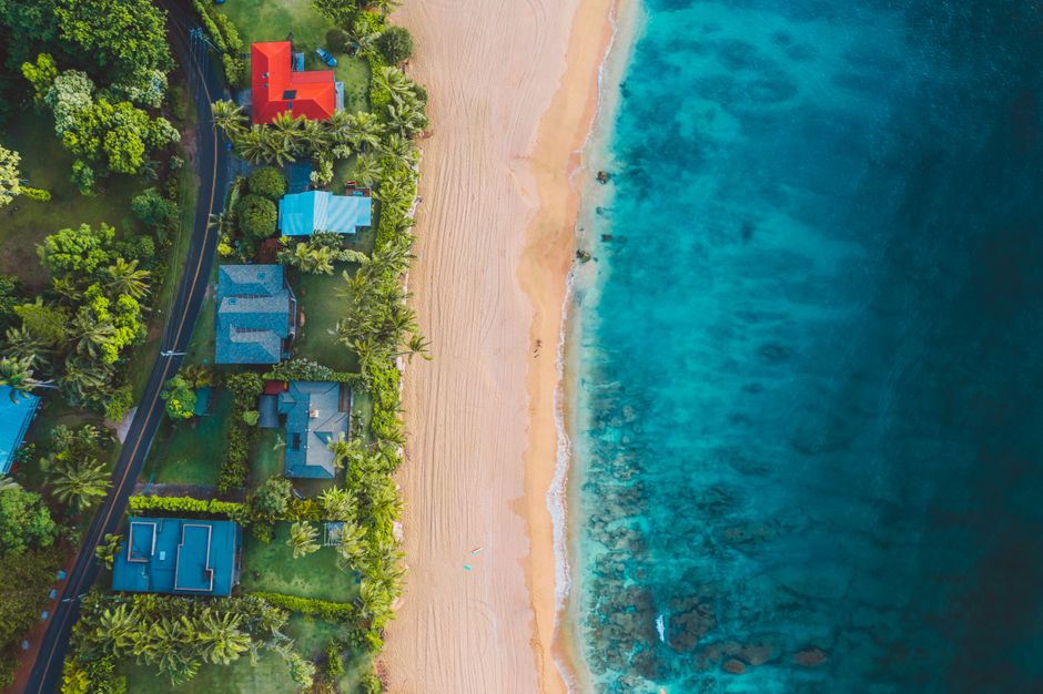 Spectacular West Maui and Molokai with Oceanfront Landing Helicopter Tour Review Review 2026 - Stunning aerial shot of a tropical beach, turquoise sea, and palm-lined coastal homes.