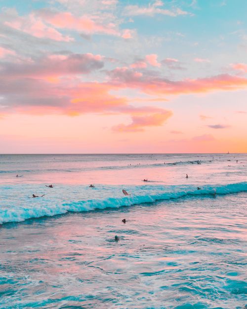 Free A beautiful pastel-colored sunset over a calm ocean with people swimming gently in the waves. Stock Photo