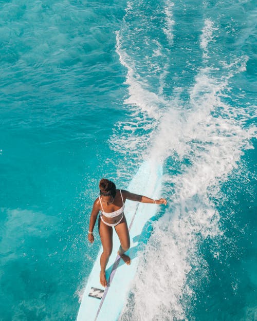 Woman in White Bikini Standing on White Surfboard on Blue Sea