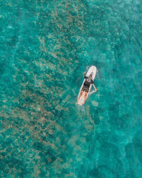 Free A surfer paddling on a surfboard over vibrant blue ocean water. Perfect for adventure and travel themes. Stock Photo
