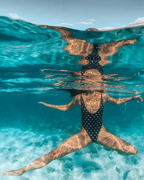 Free Woman in a swimsuit gracefully swimming underwater with legs apart. Stock Photo