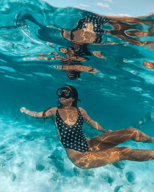 Free A woman in a patterned swimsuit and dive mask swims gracefully underwater in clear water. Stock Photo